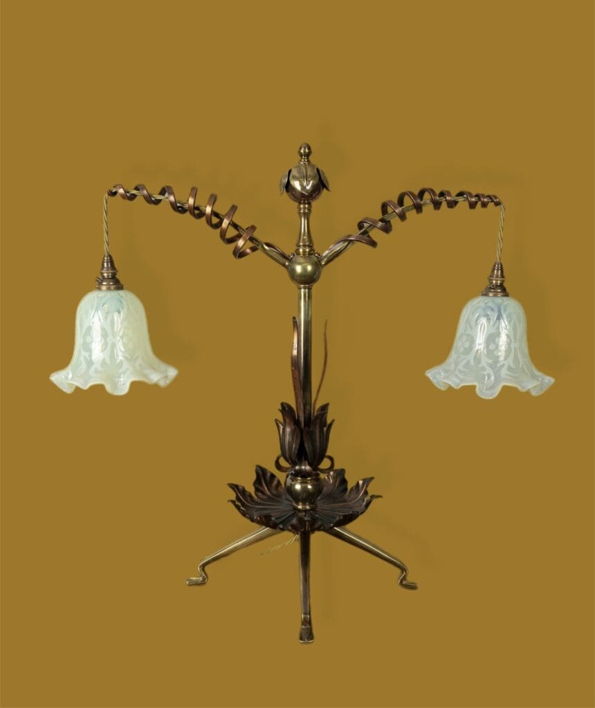 An original William Benson table lamp.  Highly decorative and featuring spiral scrolls on the twin arms which suspend delicate vaseline glass shades